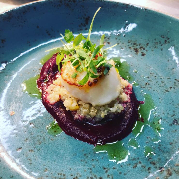 A blue plate featuring a beautifully arranged scallop garnished with vibrant beetroot slices. A blue plate featuring a beautifully arranged scallop garnished with vibrant beetroot slices.